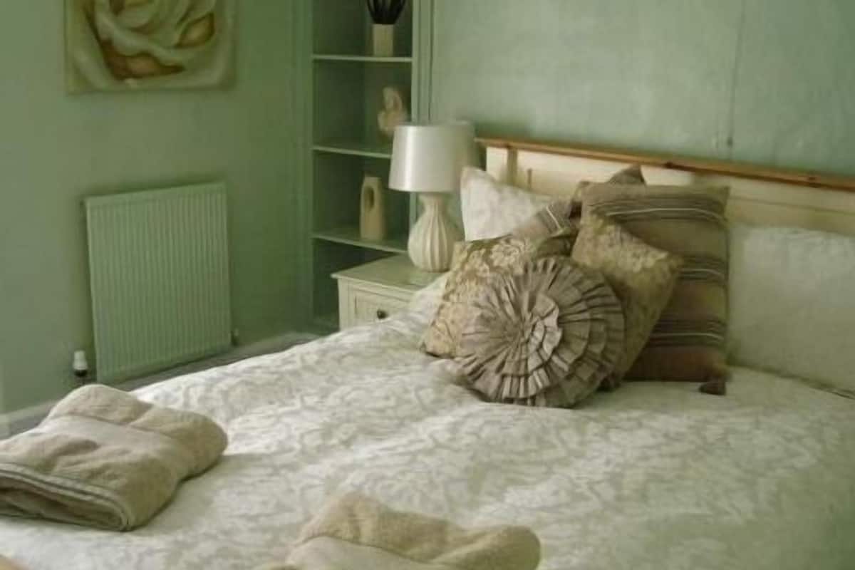 A bedroom with a bed, pillows, a nightstand, a lamp, and a radiator.