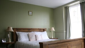 A bedroom with a wooden bed, two bedside tables with lamps, a green wall, and a window with curtains. - The Pack Horse (South Brent)