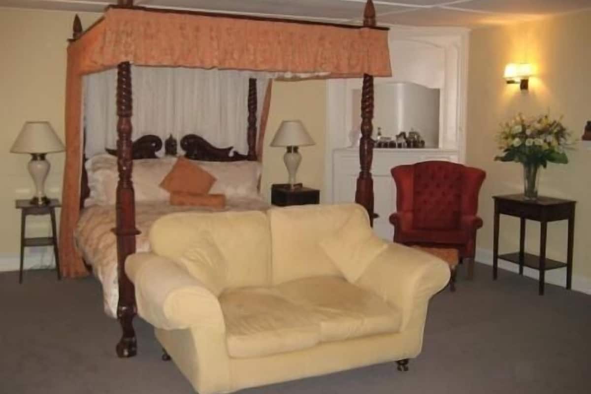 A four-poster canopy bed with a red chair and a small table beside it.