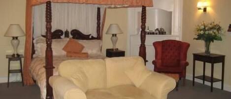 A four-poster canopy bed with a red chair and a small table beside it.