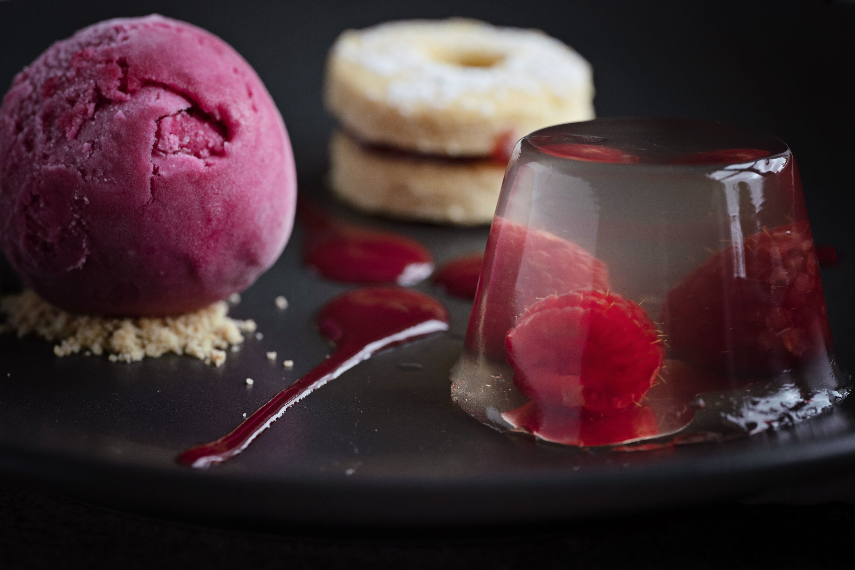 Een dessertbord met een bol roze ijs, een heldere kwark met aardbeien, en een donut.