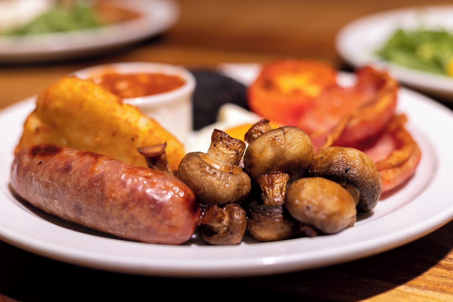 Une assiette de nourriture comprenant des saucisses, des champignons et une pomme de terre au four.