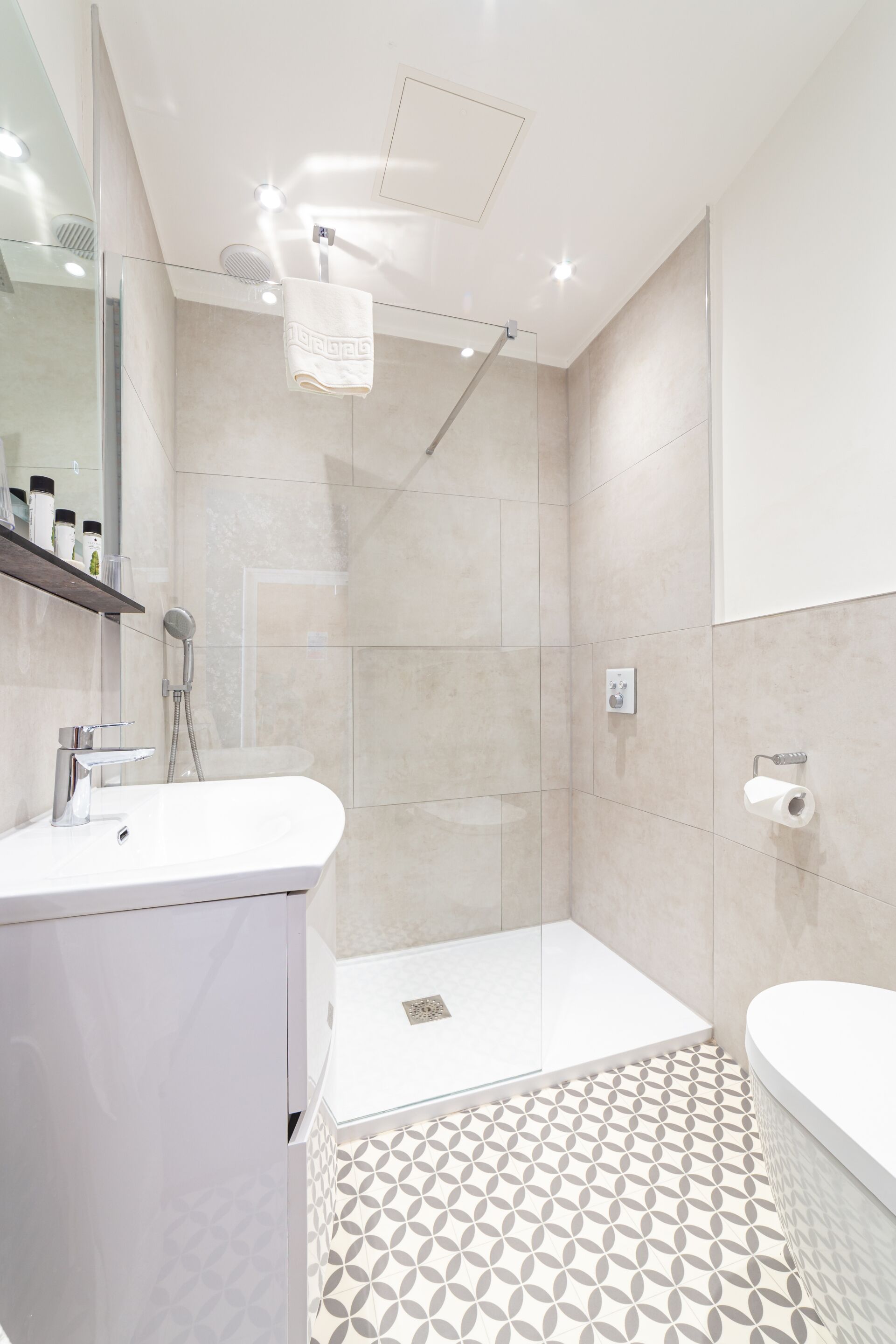 A modern bathroom with a glass shower enclosure, a white sink, and a patterned floor.
