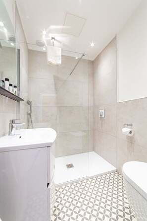 A modern bathroom with a glass shower enclosure, a white sink, and a patterned floor.
