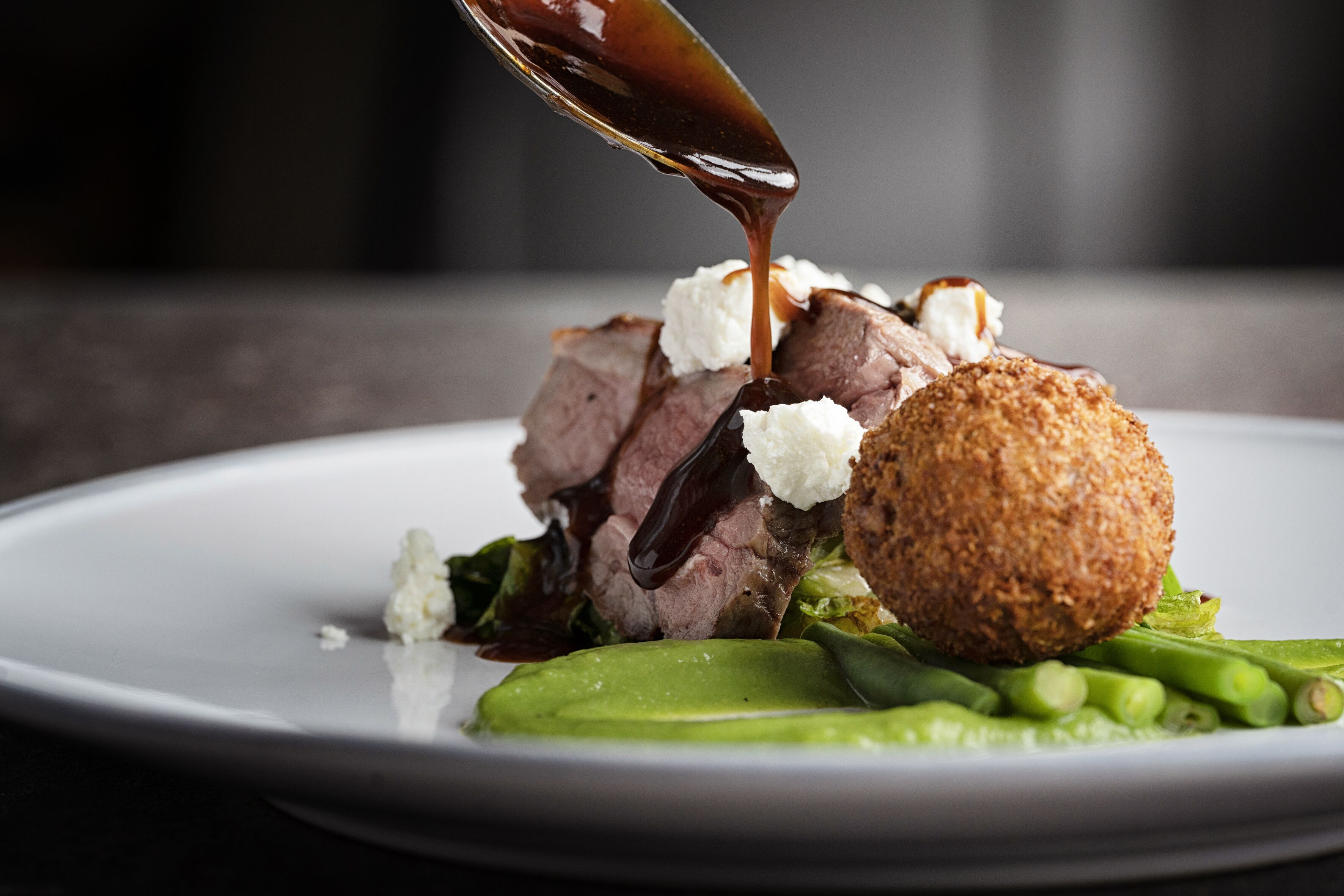 A plated dish with meat, a round breaded item, and green vegetables.