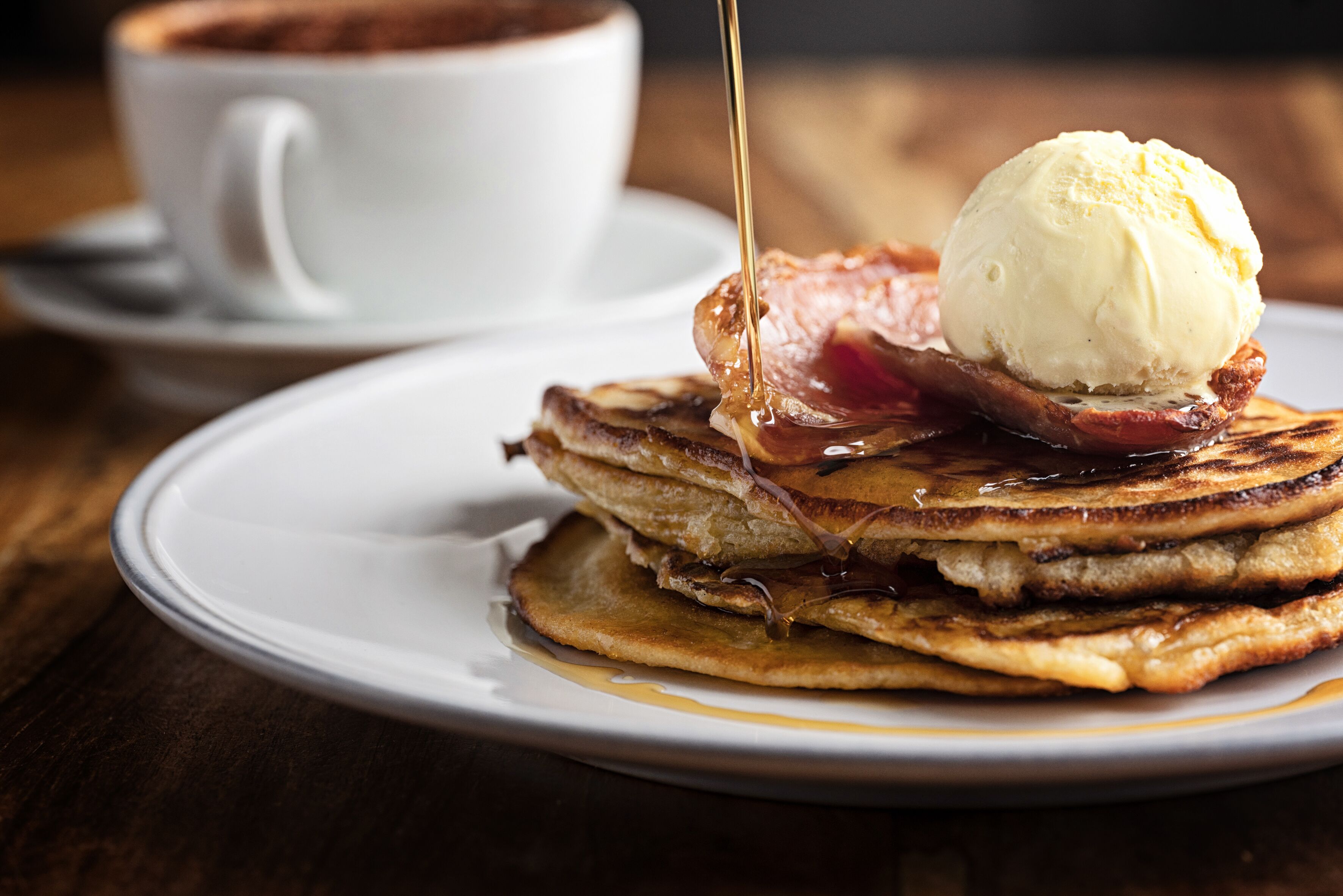 A stack of pancakes with syrup and a scoop of ice cream on a plate.