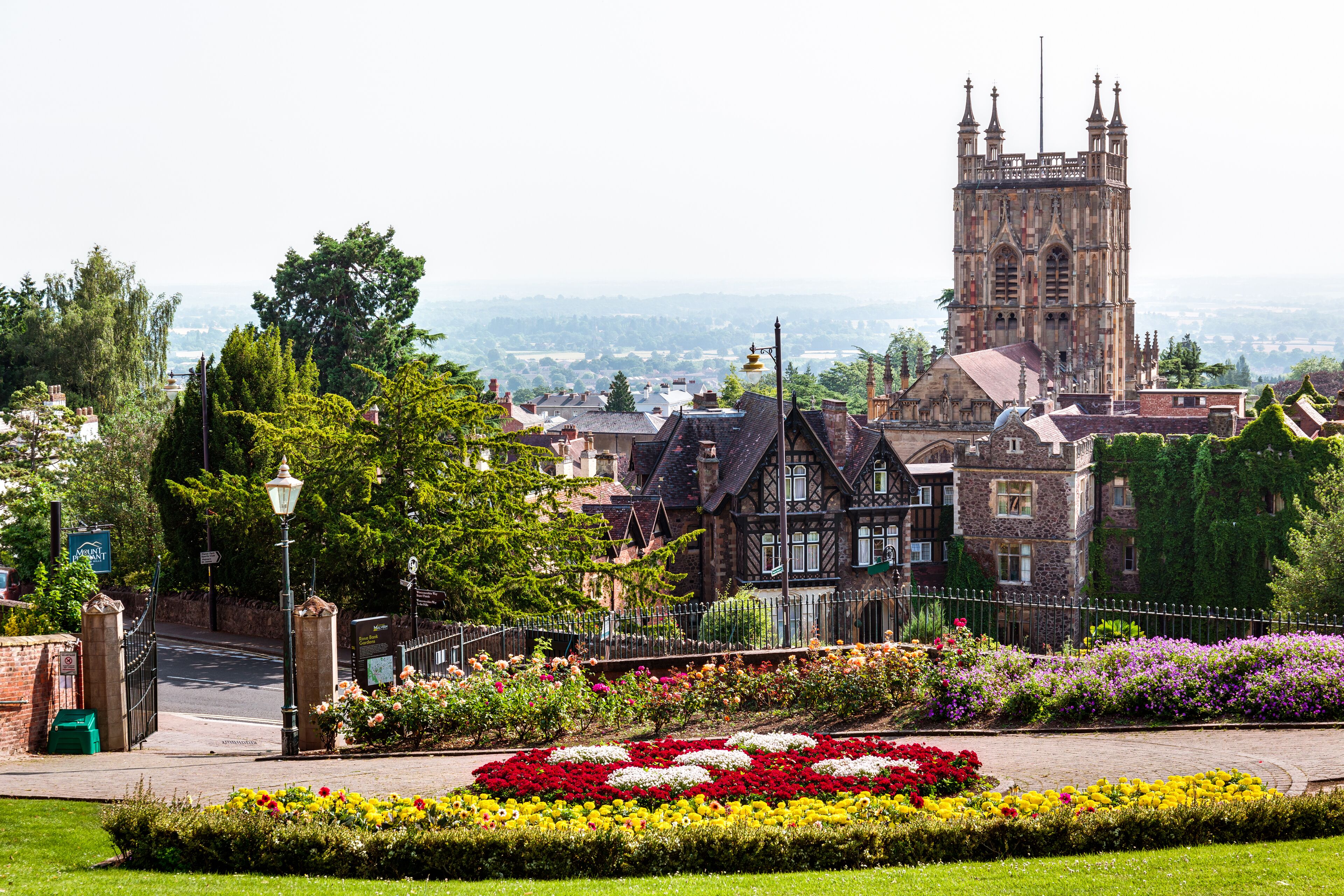 A historic building with a prominent tower, surrounded by well-maintained gardens and a paved walkway.