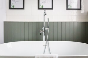 A modern bathroom with a freestanding bathtub, framed artwork on the wall, and a green paneling design. - The Mount Pleasant Hotel (Malvern)