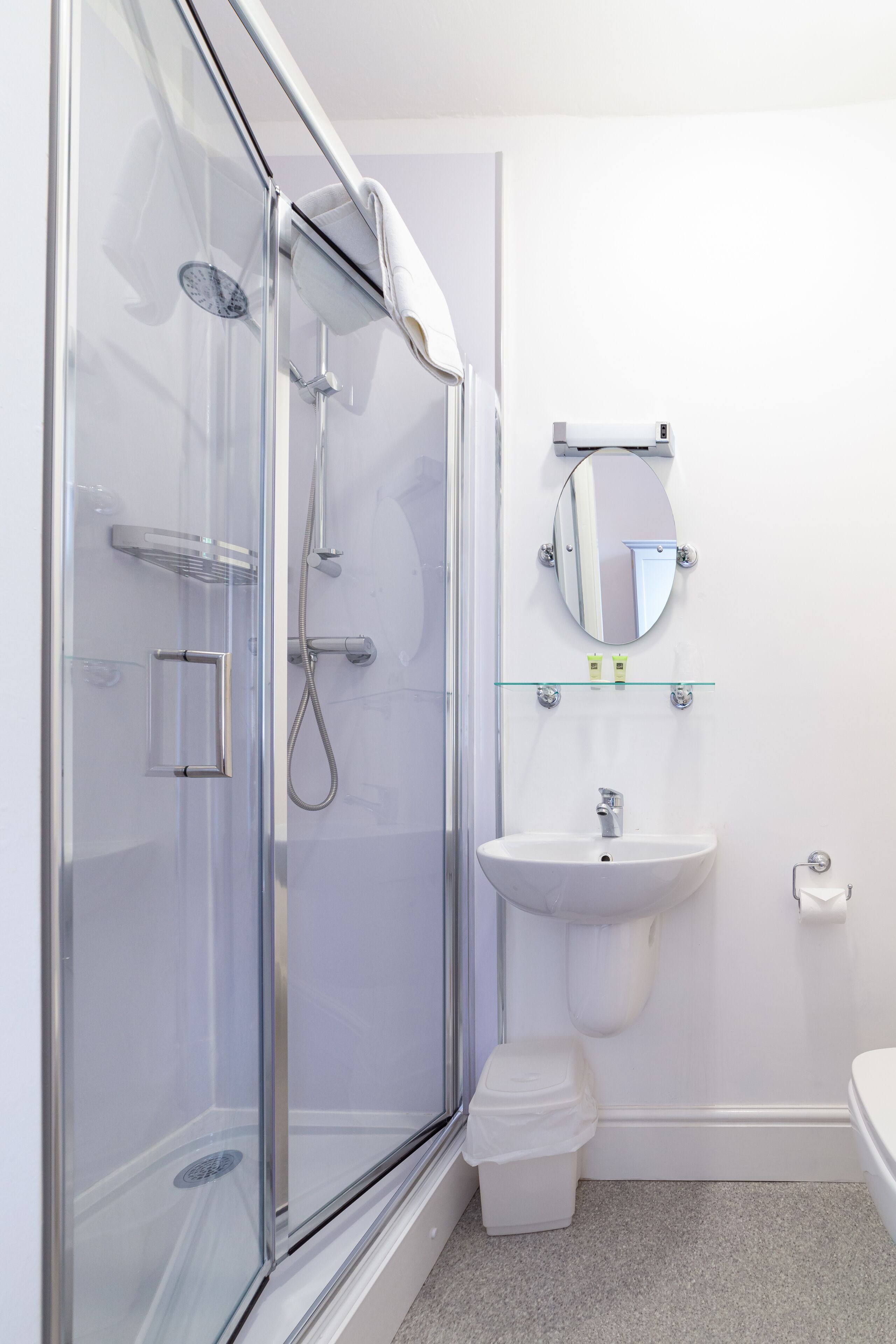 Un baño moderno con ducha envuelta en vidrio, lavamanos blanco y un inodoro.