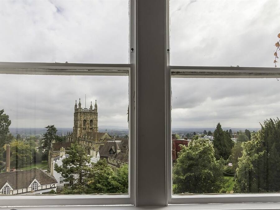 A view through a window of a historic building with a prominent tower, surrounded by greenery and other buildings.