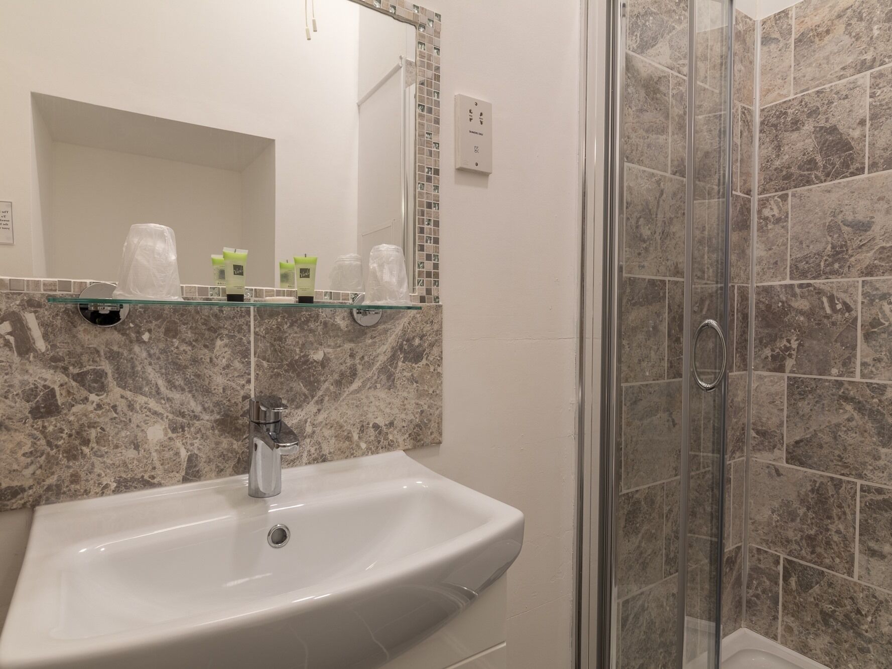 A bathroom with a white sink, a glass shower enclosure, and a marble-tiled shower wall.