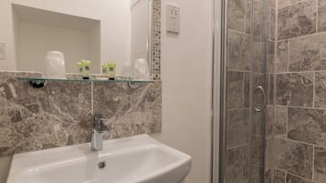 A bathroom with a white sink, a glass shower enclosure, and a marble-tiled shower wall.