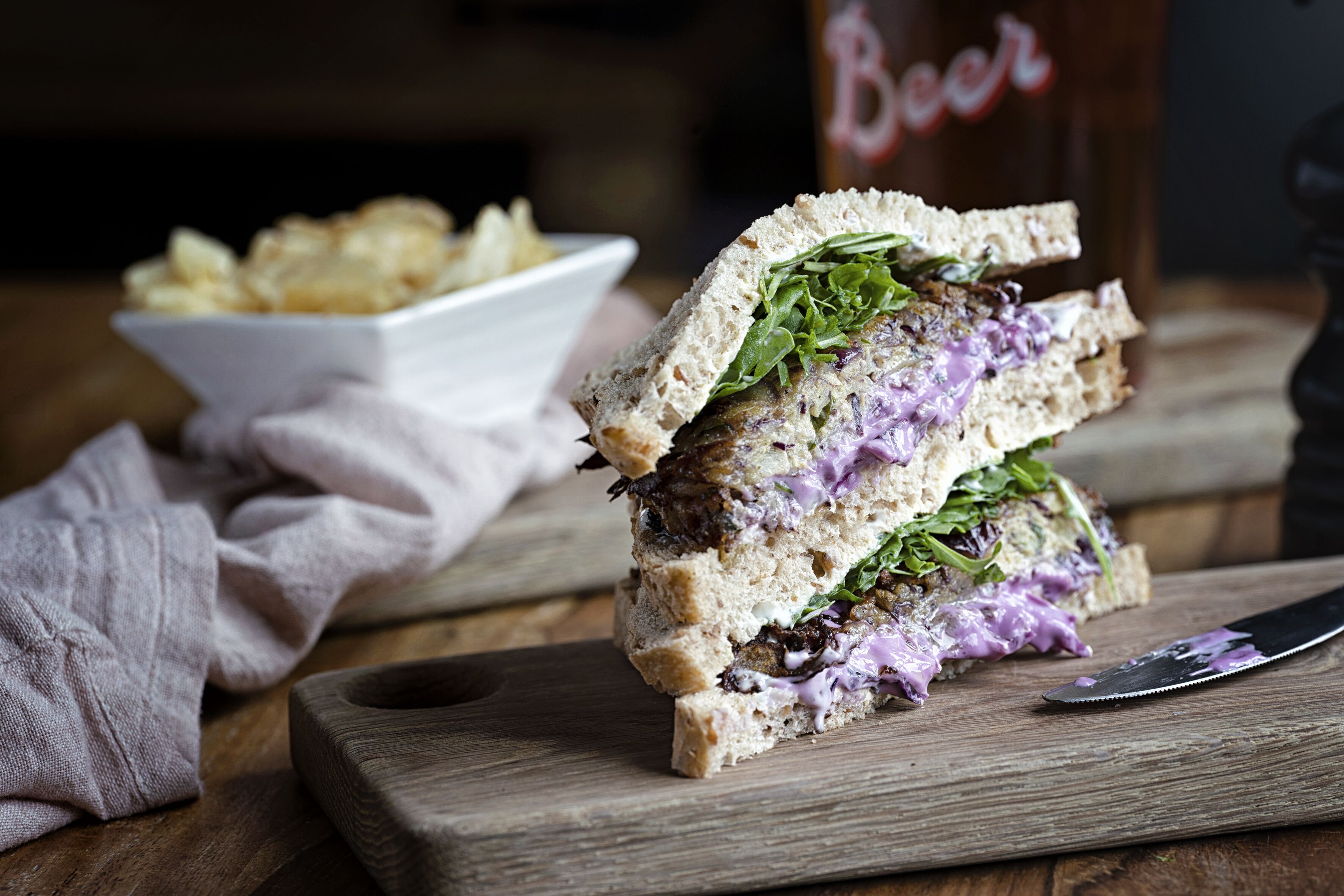 A sandwich on a wooden board with a knife beside it.