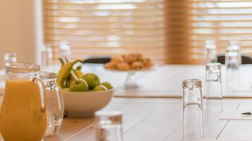 A breakfast table with a pitcher of orange juice, a bowl of green apples, and salt and pepper shakers.