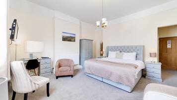 A bedroom with a large bed, a desk, a chair, and a wardrobe.