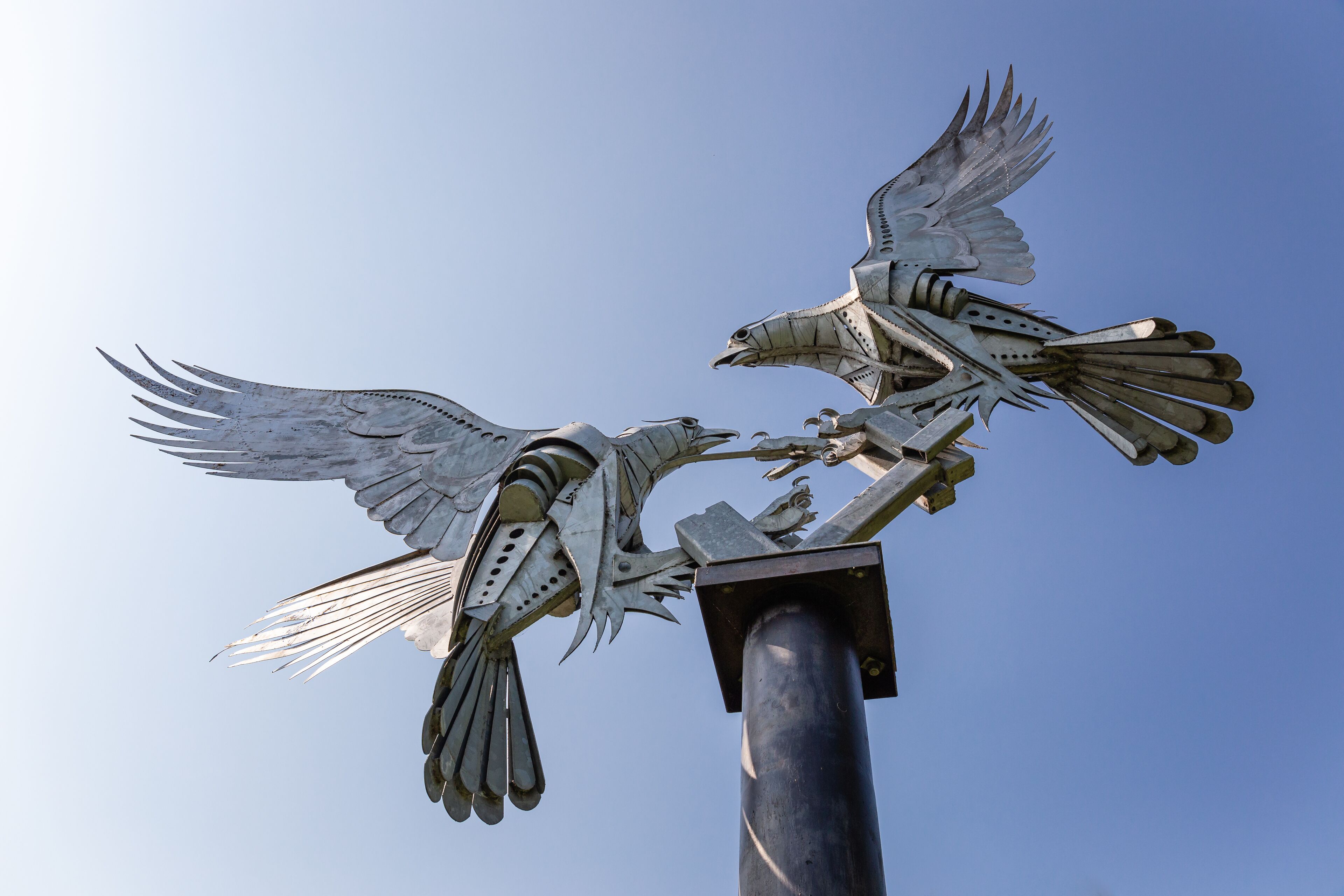 A metal sculpture of two birds in flight, mounted on a pole.