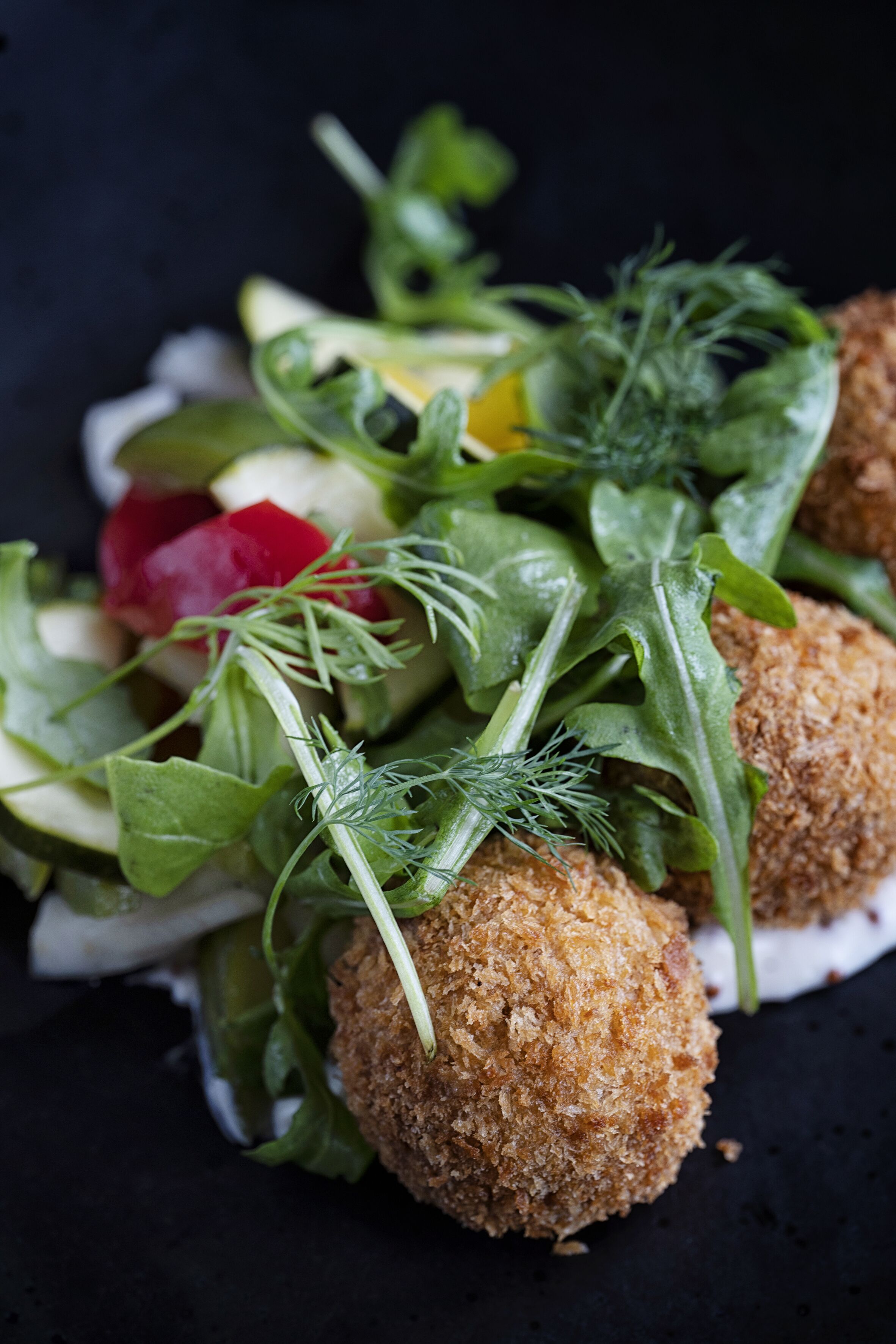 A close-up of a food dish with breaded balls, greens, and radishes.