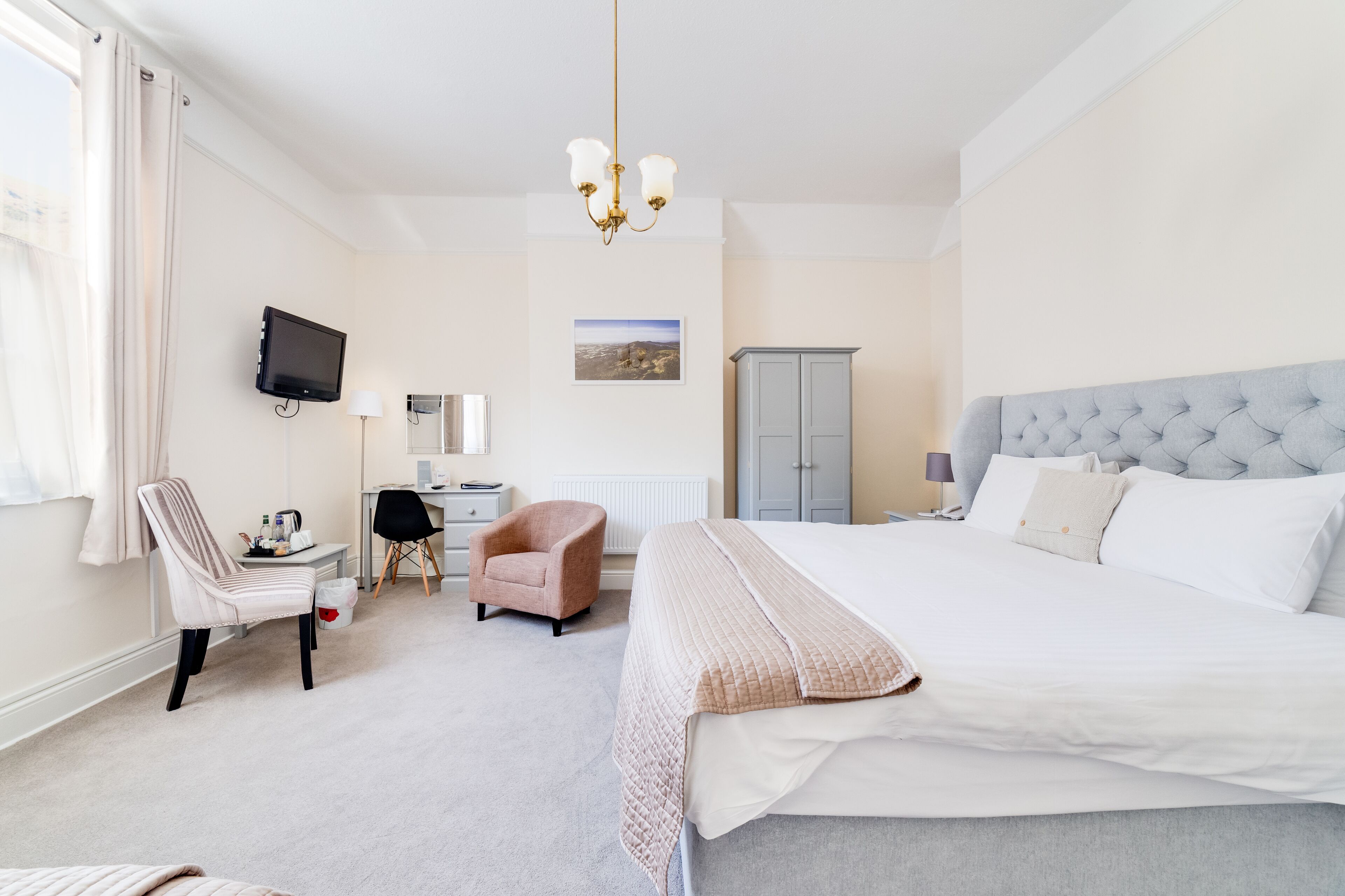 Une chambre d’hôtel avec un grand lit, un bureau avec une chaise, une télévision, une armoire et une fenêtre avec des rideaux.