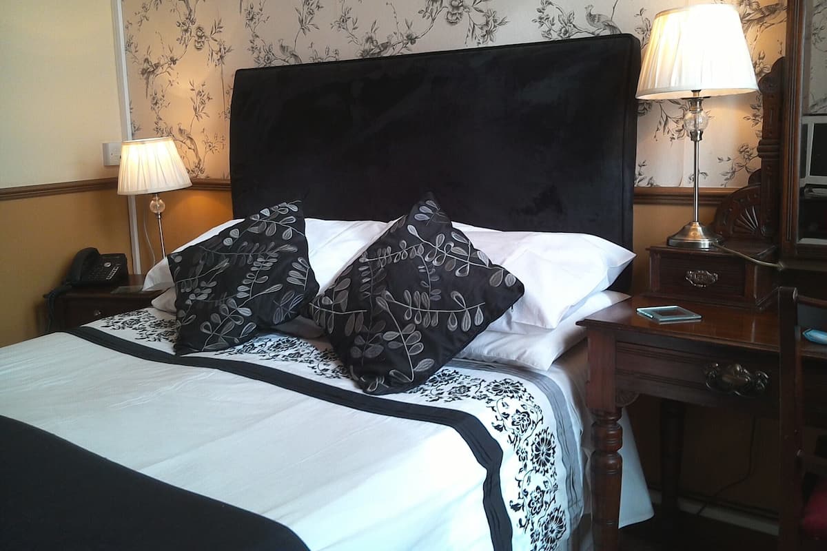 Una cama bien hecha con almohadillas estampadas en blanco y negro, un cabecero oscuro y dos lámparas de noche.