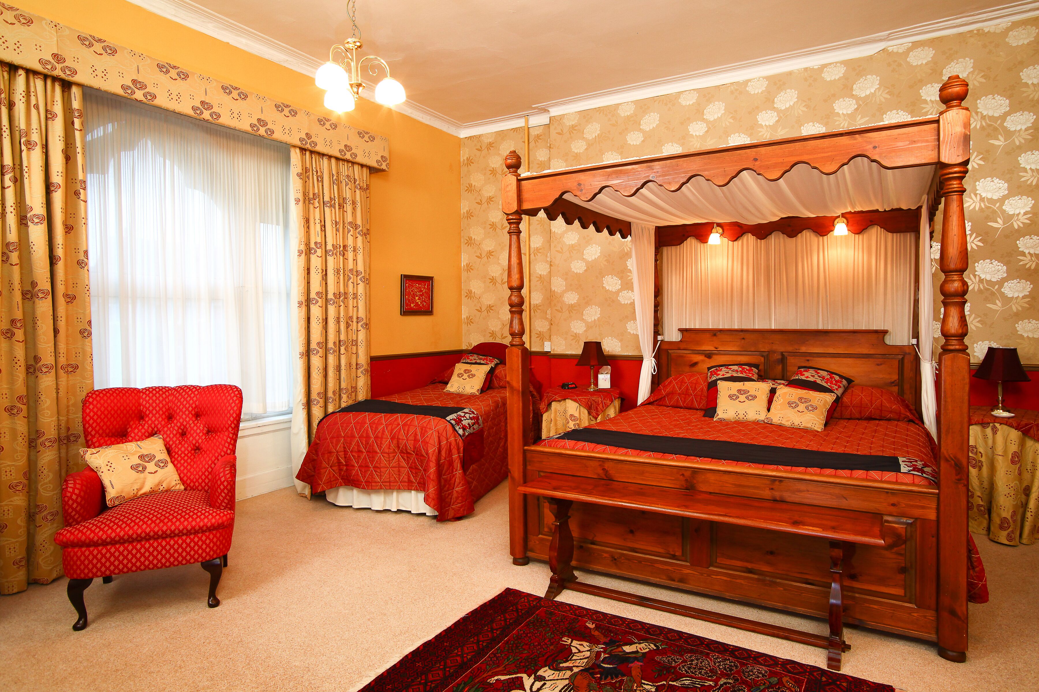 A traditional four-poster bed with a canopy, two bedside tables, and a red armchair.