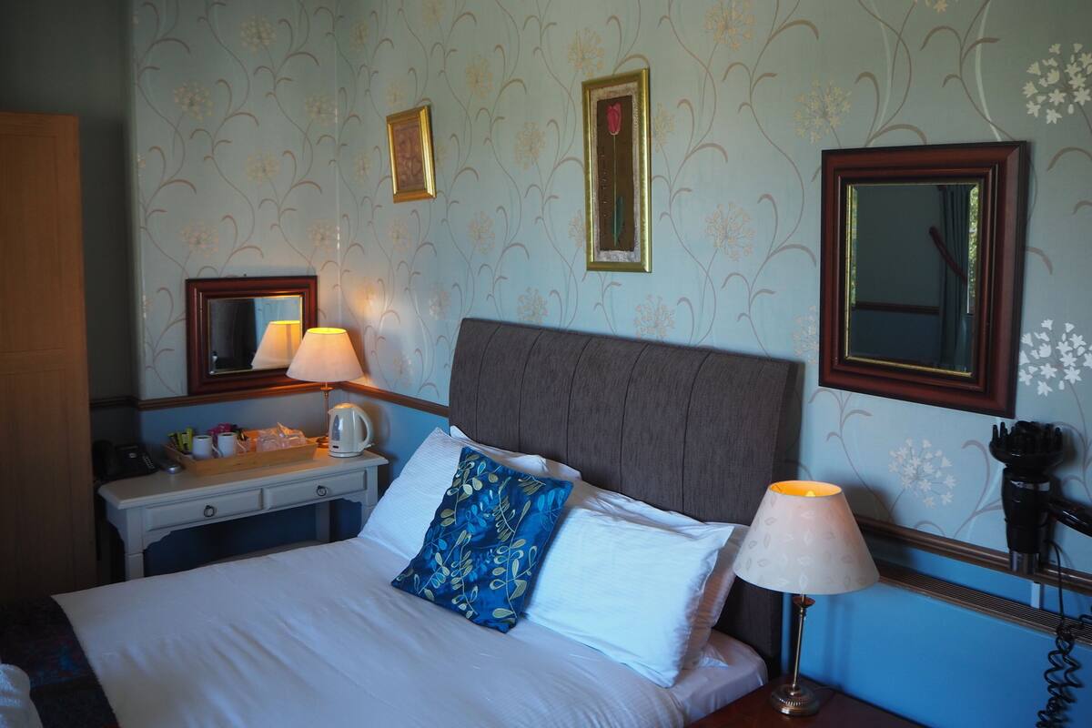 Una habitación de hotel con cama, mesita de noche, lámpara y paneles decorativos en la pared.