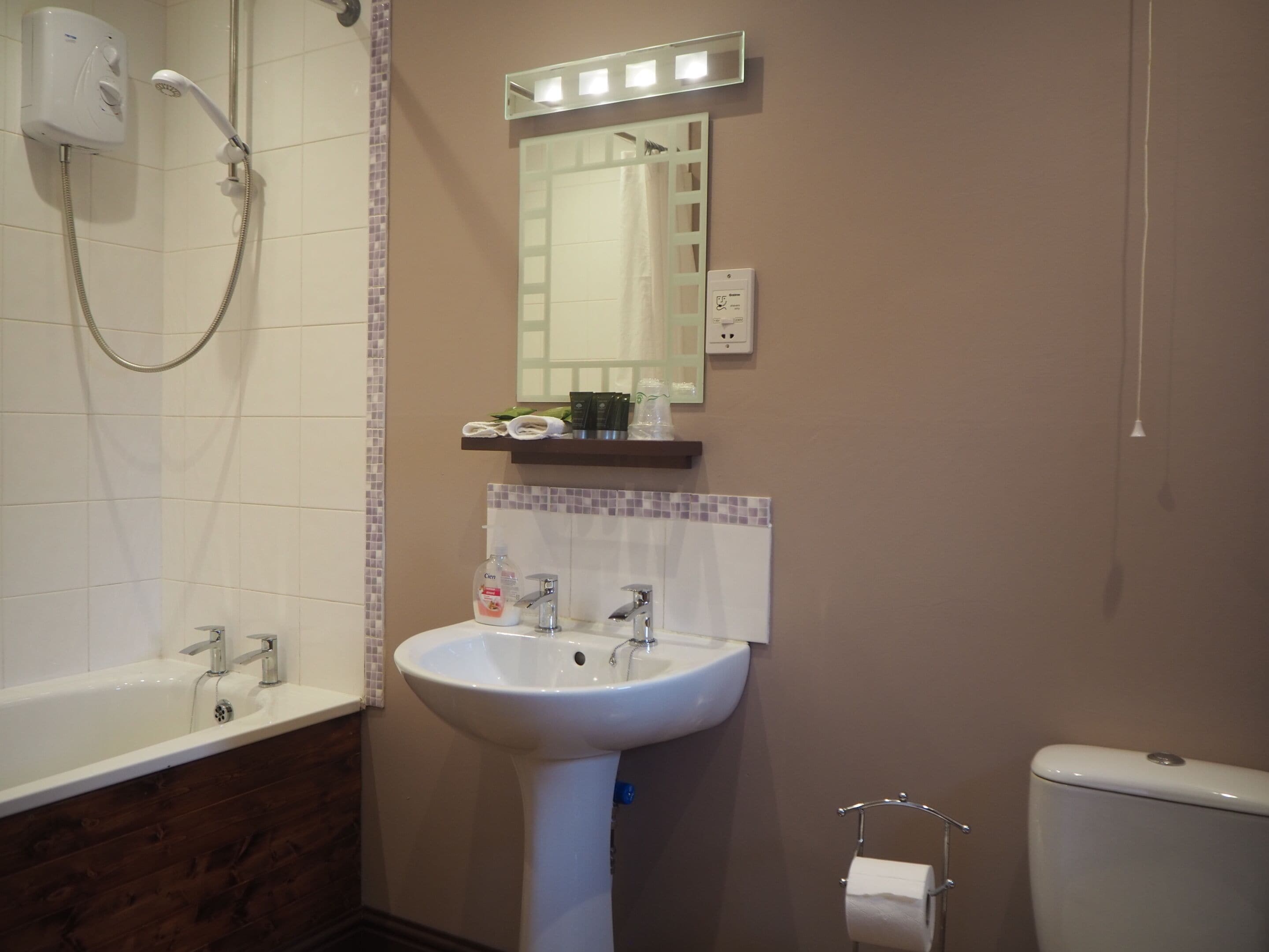 Et badeværelse med en hvid vask, brusebad, spejl og toilet.