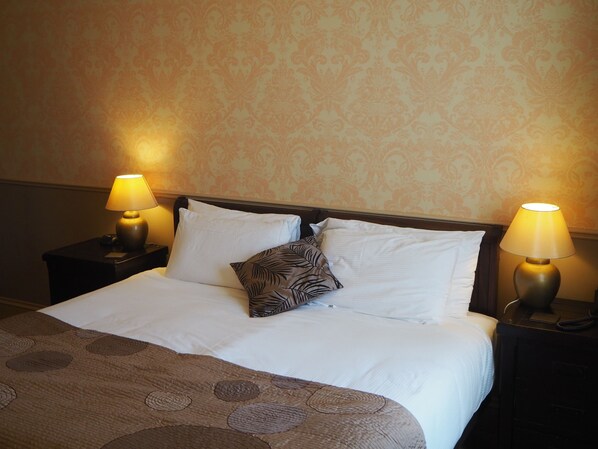 A neatly made bed with white linens and a patterned throw, flanked by two bedside tables with lamps, set against a wallpapered wall.