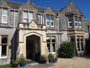 A historic stone building with a prominent entrance, multiple windows, and potted plants in the foreground. - Meare Manor (Glastonbury)