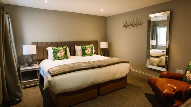 Una habitación de hotel con una cama grande, una mesita de noche, un espejo y un sillón de cuero marrón.