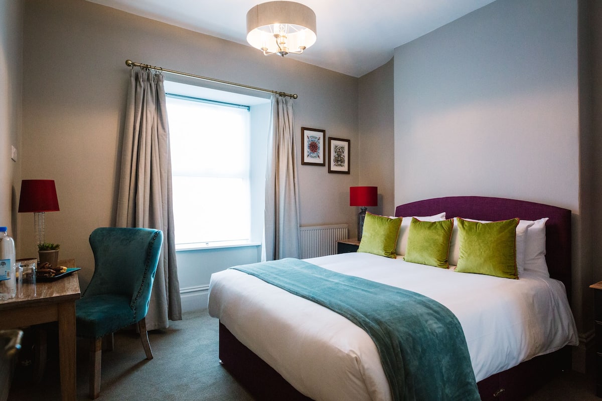 A hotel room with a bed, a desk, a chair, and a window with curtains.