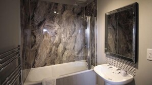 Un baño moderno con pared de ducha de mármol, una bañera independiente y un lavamanos empotrado.