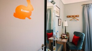 Habitación de hotel con espejo que refleja un baño, una mesa de madera con lámpara y dos sillas.