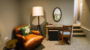 Una habitación con un sillón de cuero, un escritorio con silla, una lámpara de pie y un espejo en la pared.