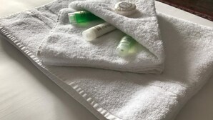 Una toalla blanca doblada con dos pequeñas botellas verdes y un tubo blanco encima.