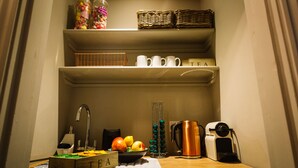 Una cocina con un lavamanos, un hervidor, una cafetera y un bol de fruta en la encimera.