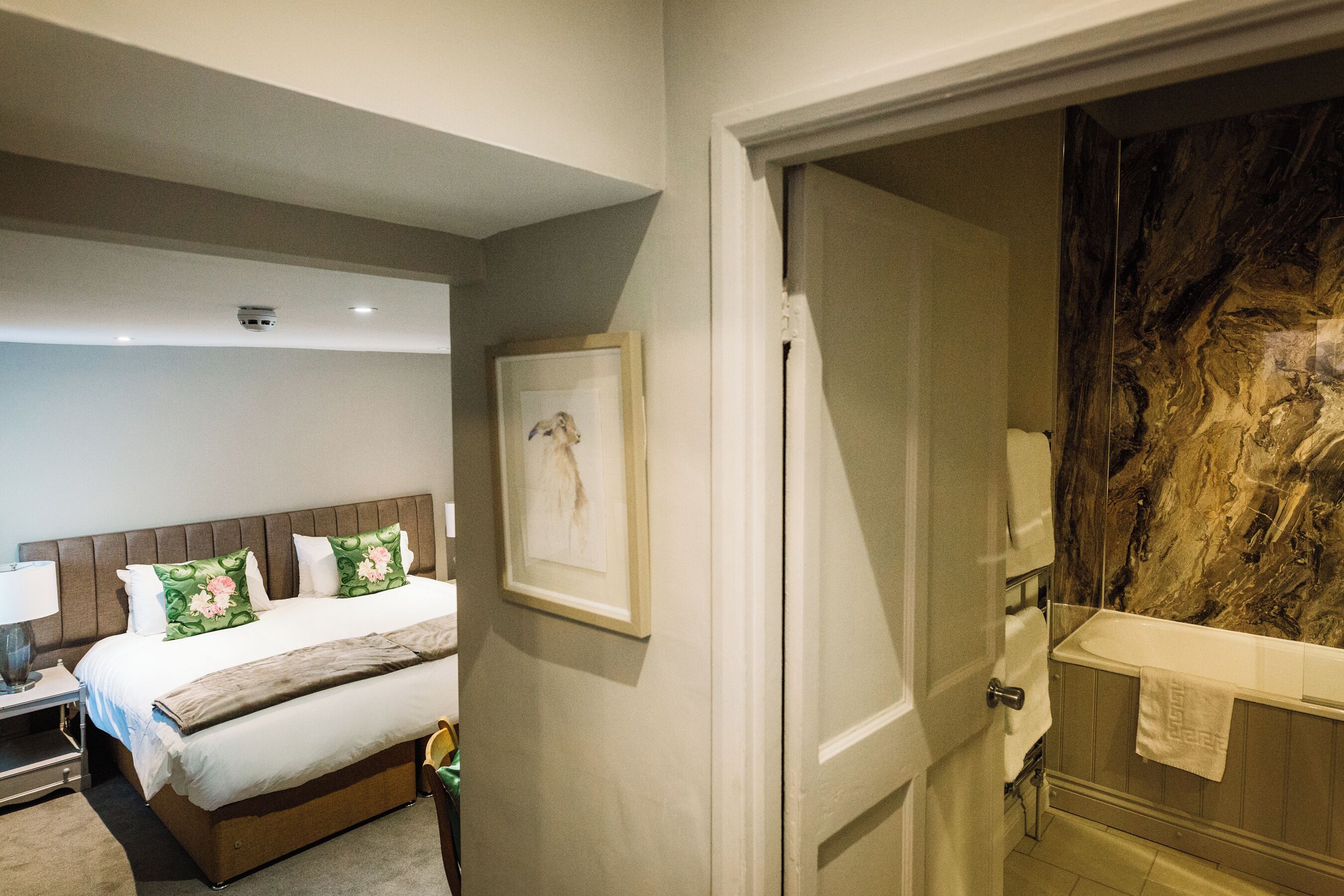 A hotel room with a bed, a framed picture on the wall, a bathroom with a marble wall, and a towel hanging on the door.