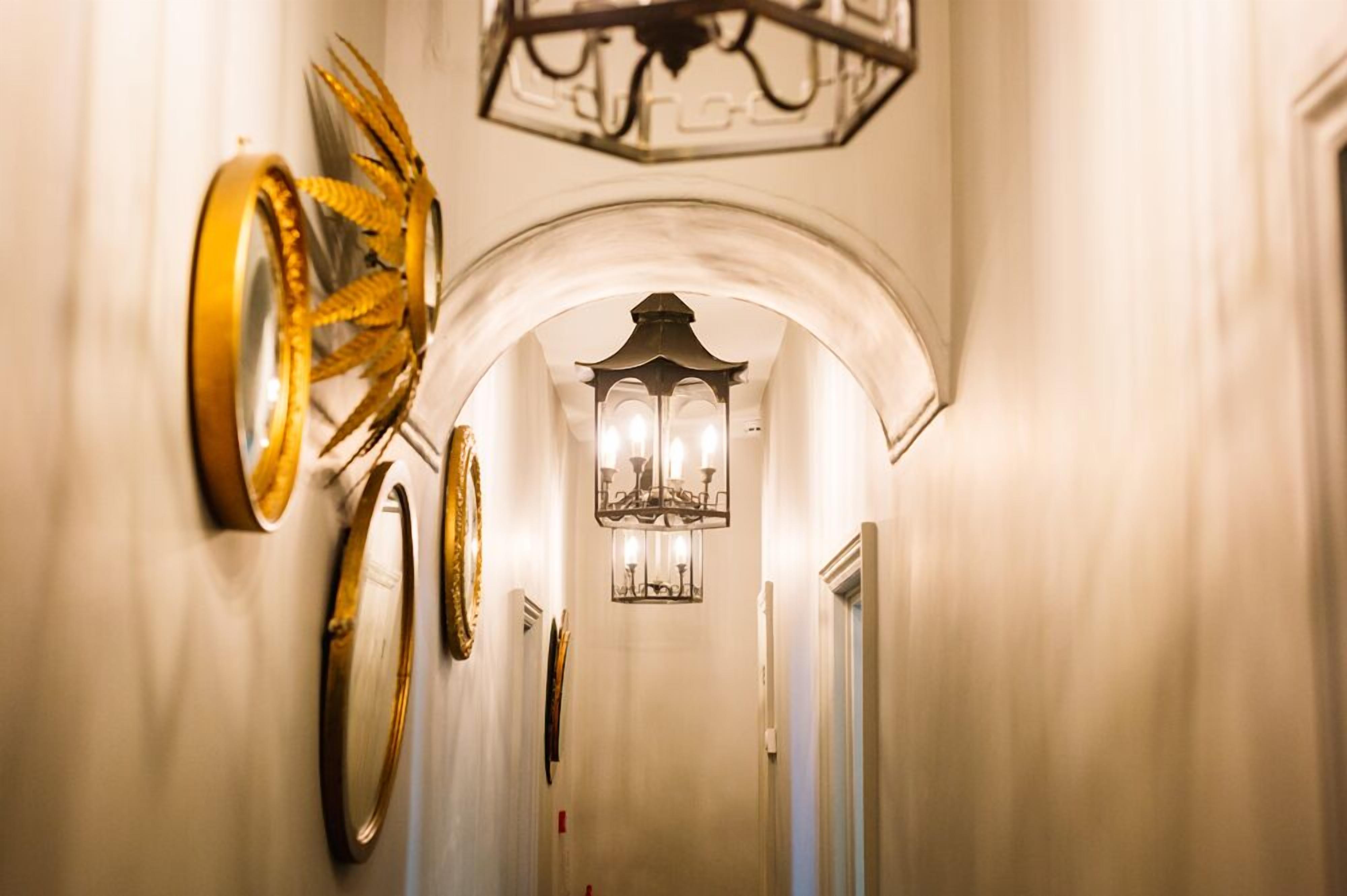 Un pasillo con candelabro, apliques de pared y espejos decorativos.