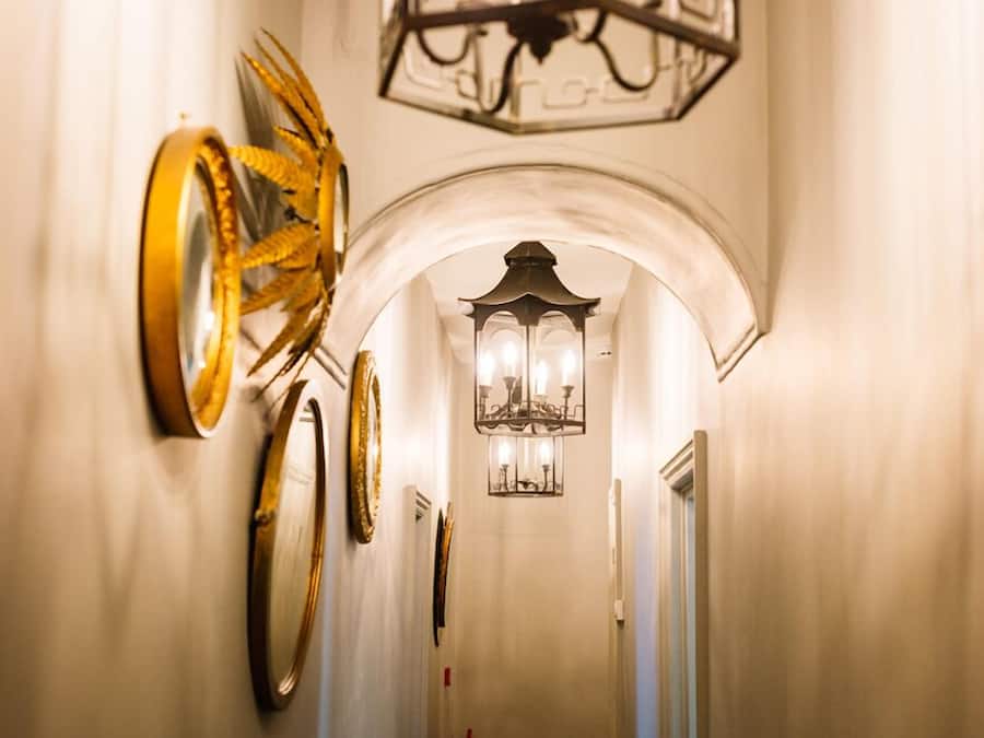 Un pasillo con candelabro, apliques de pared y espejos decorativos.