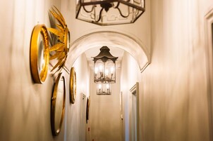 A hallway with a chandelier, wall sconces, and decorative mirrors.