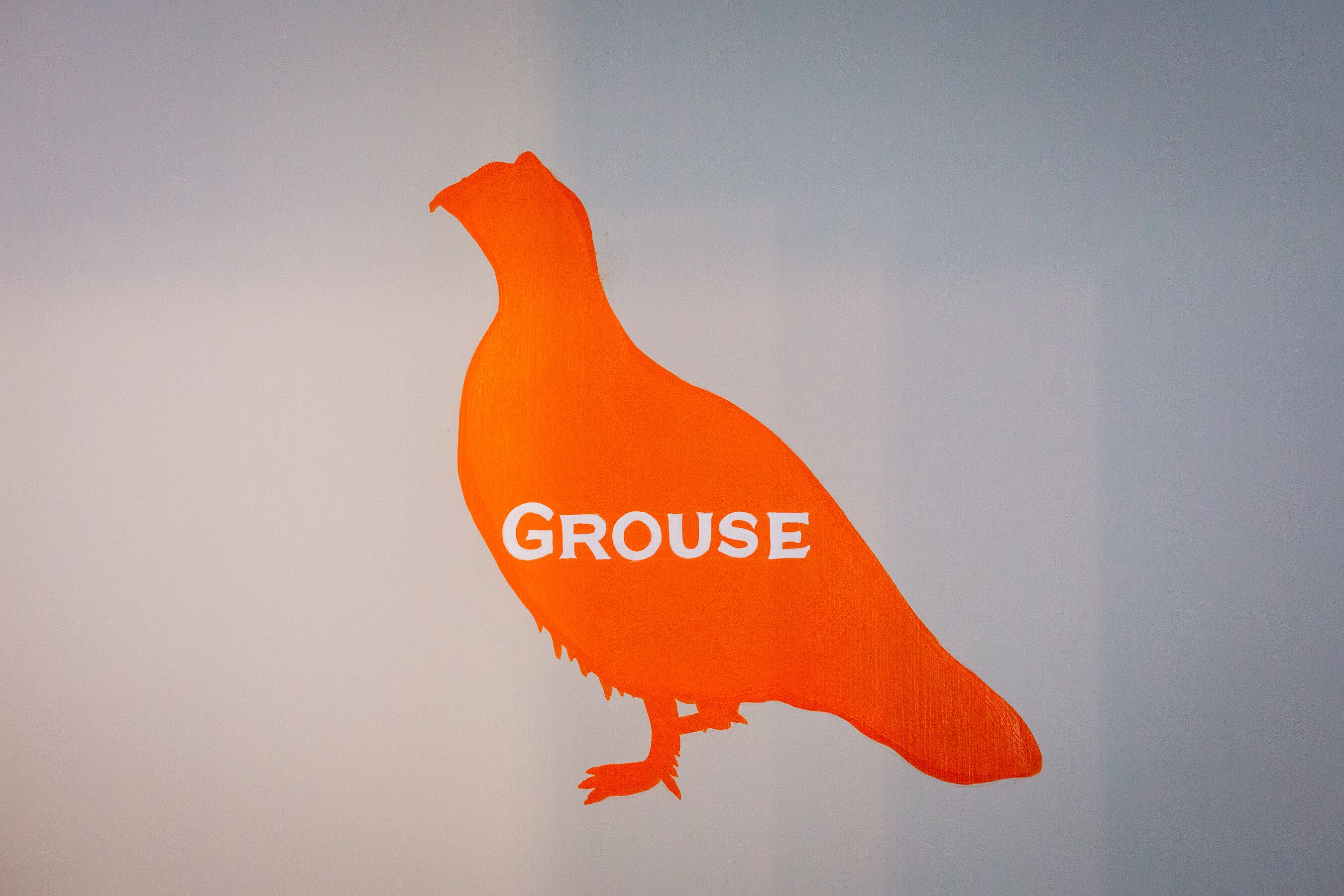 En silhuett av en skogshöna med ordet "GROUSE" på en enkel bakgrund.