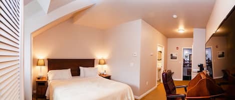 Una habitación de hotel con una cama grande, dos lámparas de noche, un cabecero de madera, una silla de madera y un escritorio con una silla.