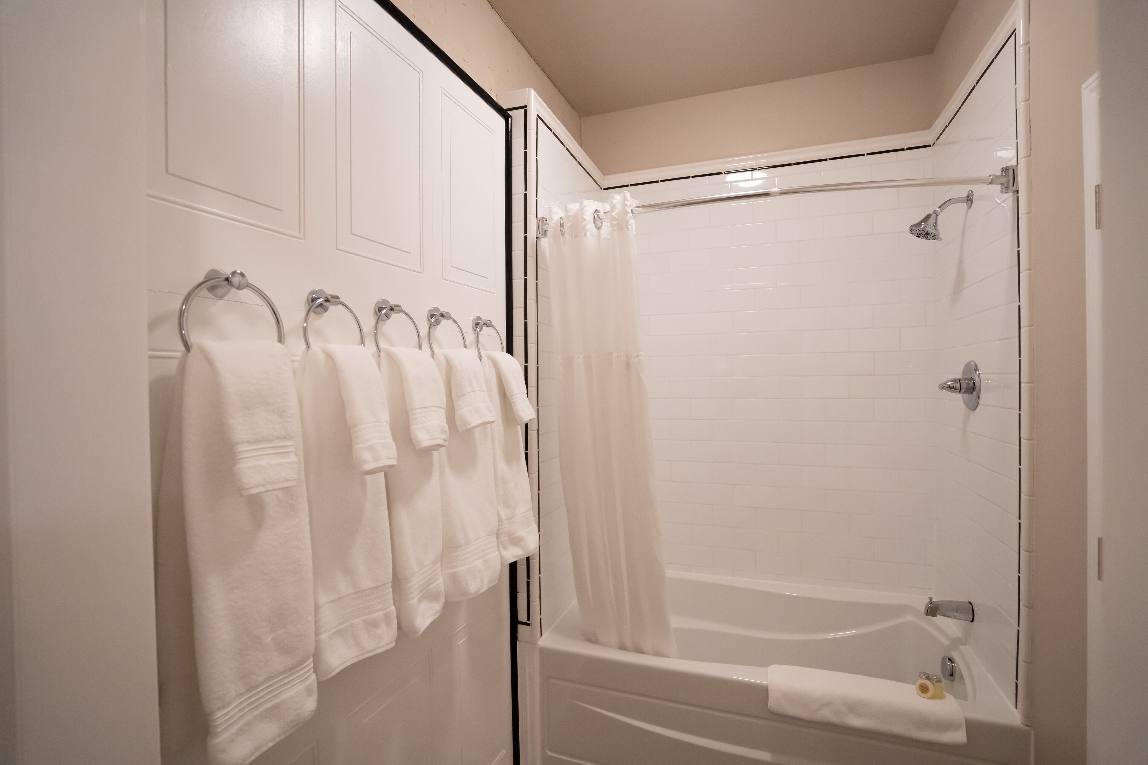 Un baño con bañera, ducha y retrete. Hay toallas colgadas en un perchero.