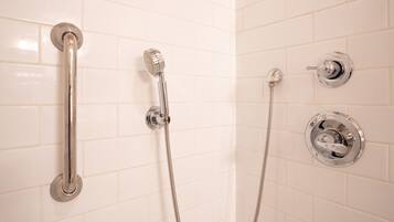 Une salle de bain avec des murs recouverts de carreaux blancs, une pomme de douche en chrome, un pommeau de douche à main et un robinet mural.
