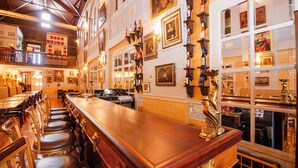 A bar area with wooden bar counter and multiple stools. There are framed pictures on the walls and a variety of bottles displayed on shelves. - Amsterdam Castle (Amsterdam)