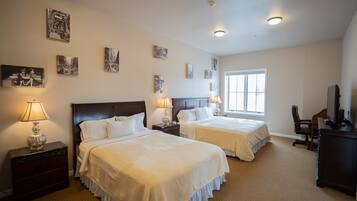 A hotel room with two beds, a desk, a chair, a TV, and artwork on the walls.