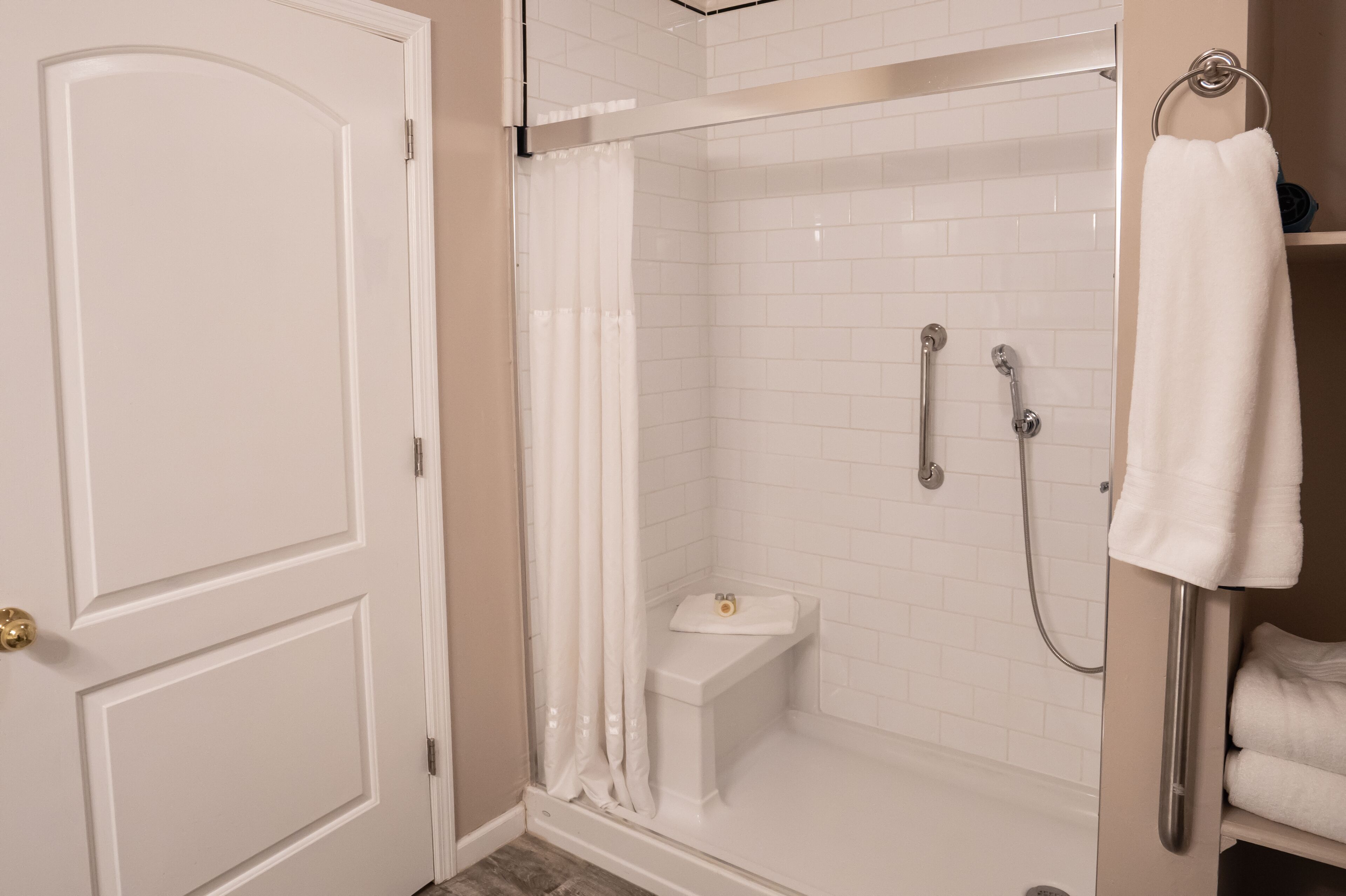 A walk-in shower with white tiles, a glass door, and a towel rack.