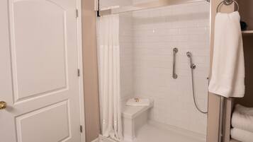 Una ducha a nivel con azulejos blancos, puerta de vidrio y un perchero.