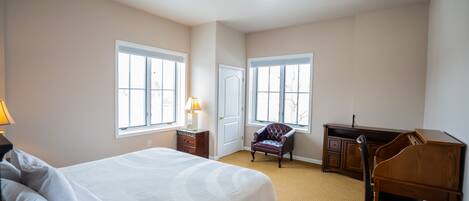A bedroom with a large bed, a desk, a chair, and two windows.