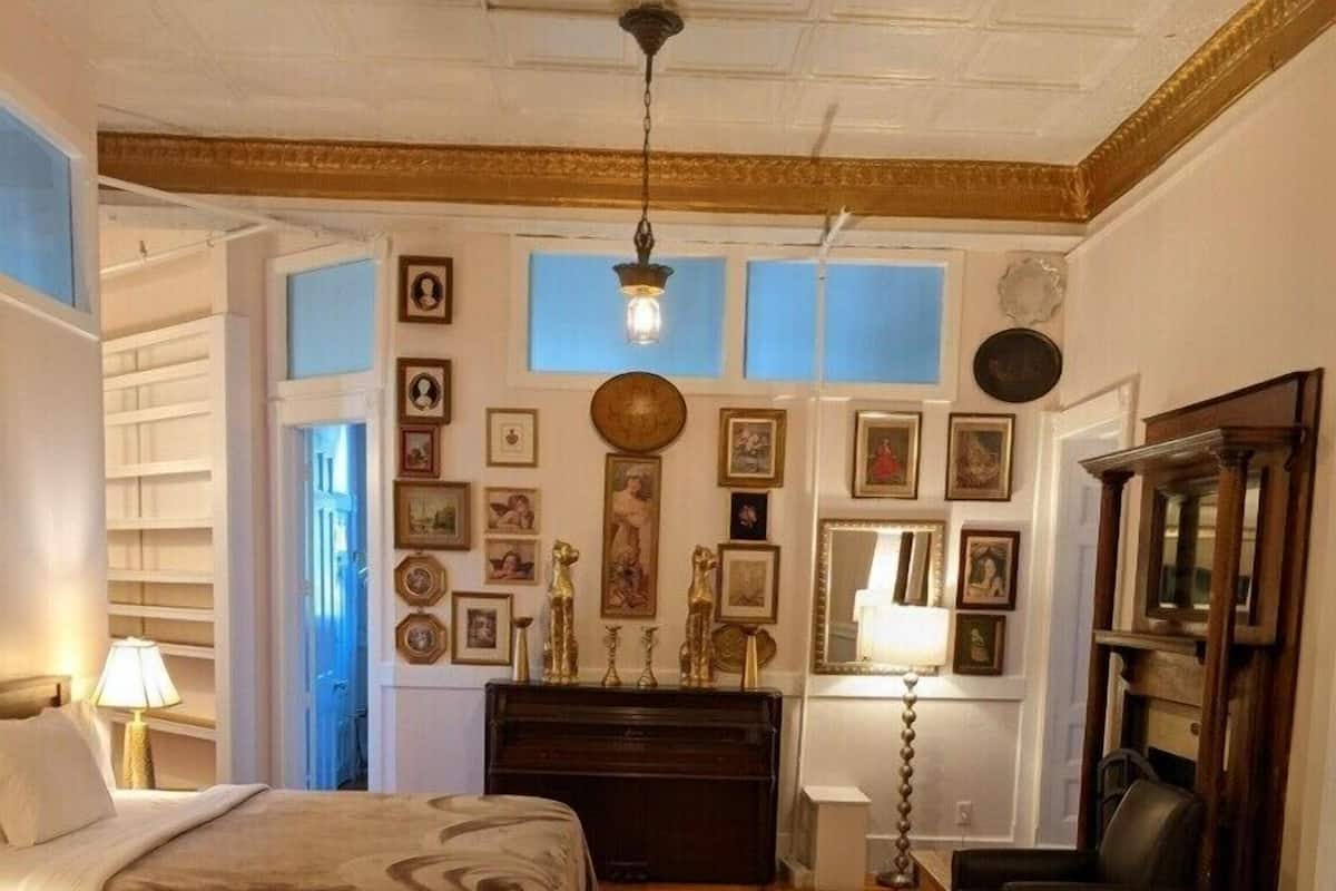 Ein Zimmer mit einem Bett, einem Schreibtisch, einem Stuhl und einer Lampe. An den Wänden hängen Bilder und auf dem Boden liegt ein Teppich.