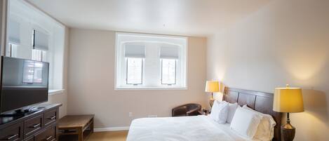 A hotel room with a bed, bedside tables, a TV, and a window with blinds.